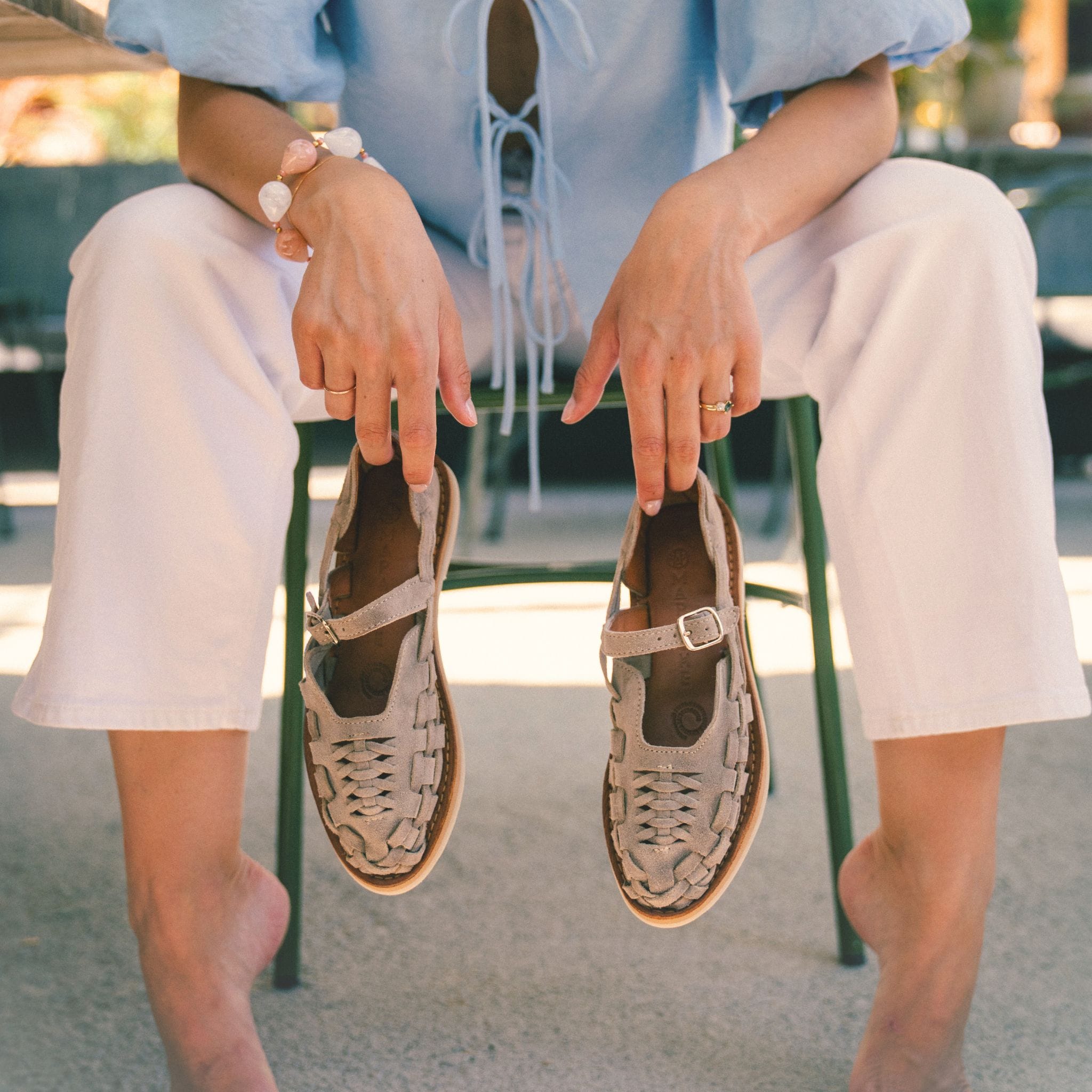 Claire est assise sur une chaise au soleil et tient dans ses mains les Gaby Suède Taupe.