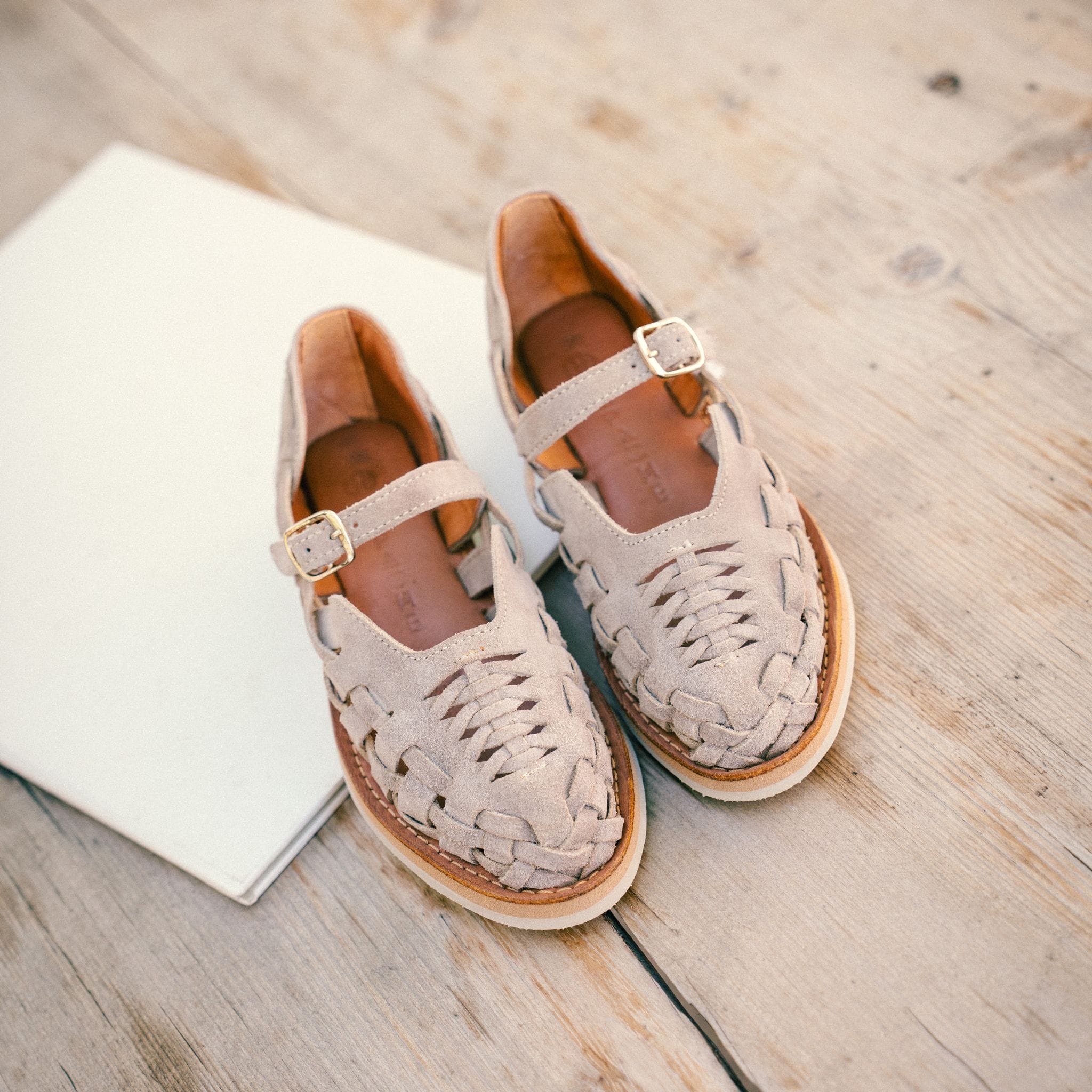 Les Gaby Suède Taupe sont posées sur une planche en bois, mettant en avant leur tressage fait à la main.