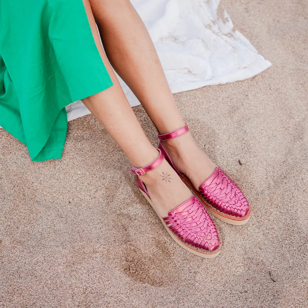 Une femme assise sur un drap blanc porte les Sandales Loma Rose Flashy dans le sable.