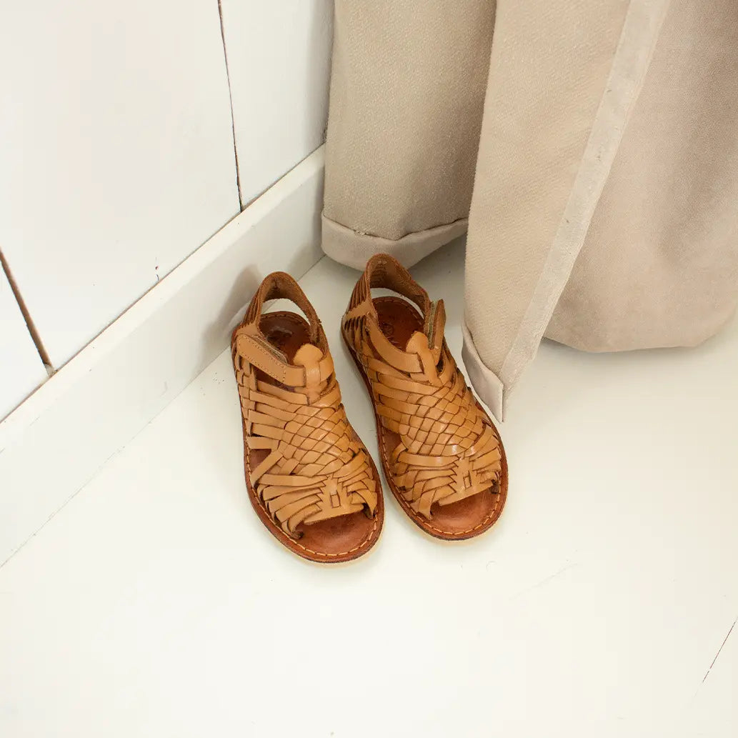 Les Sandales Sandalita Camel sont posées sur un parquet blanc à côté d'un rideau beige.