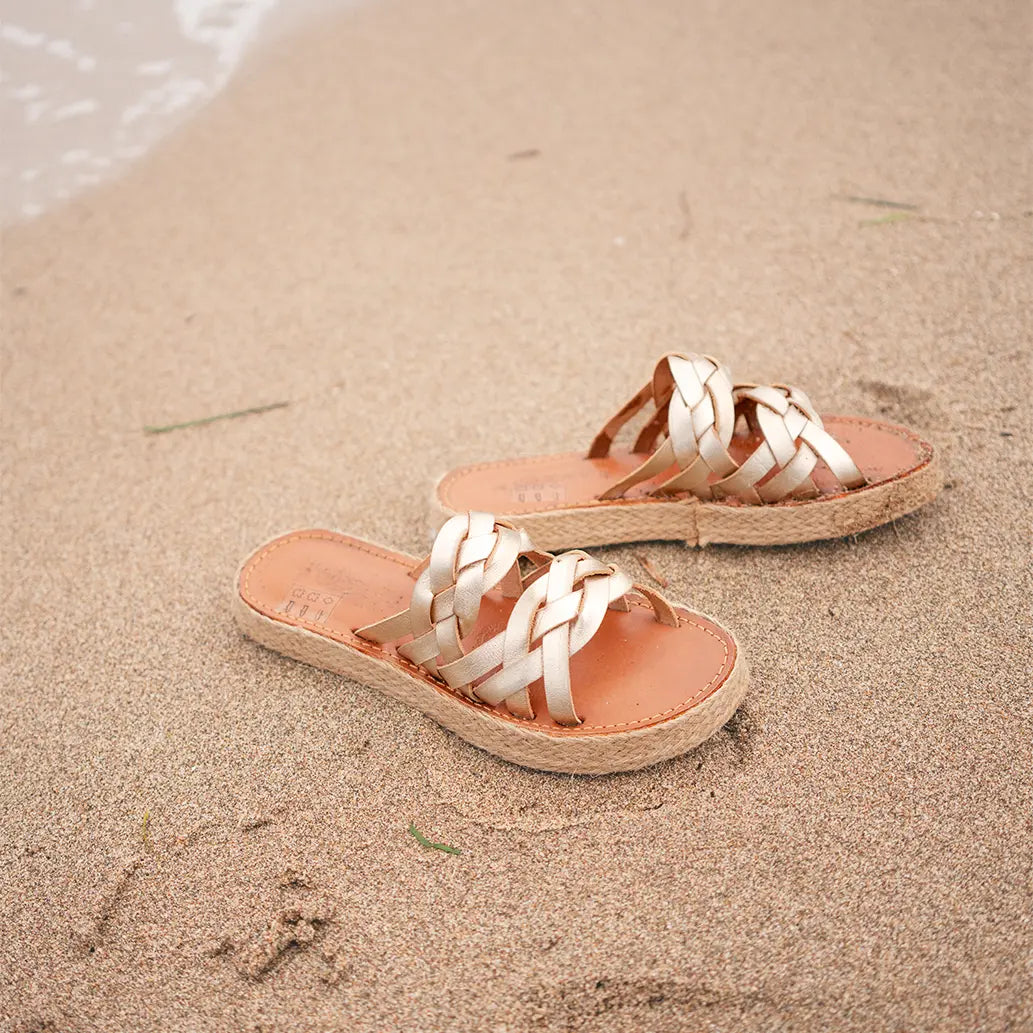 Les Mules Alma Champagnes sont posées au bord de la mer dans le sable mouillé.