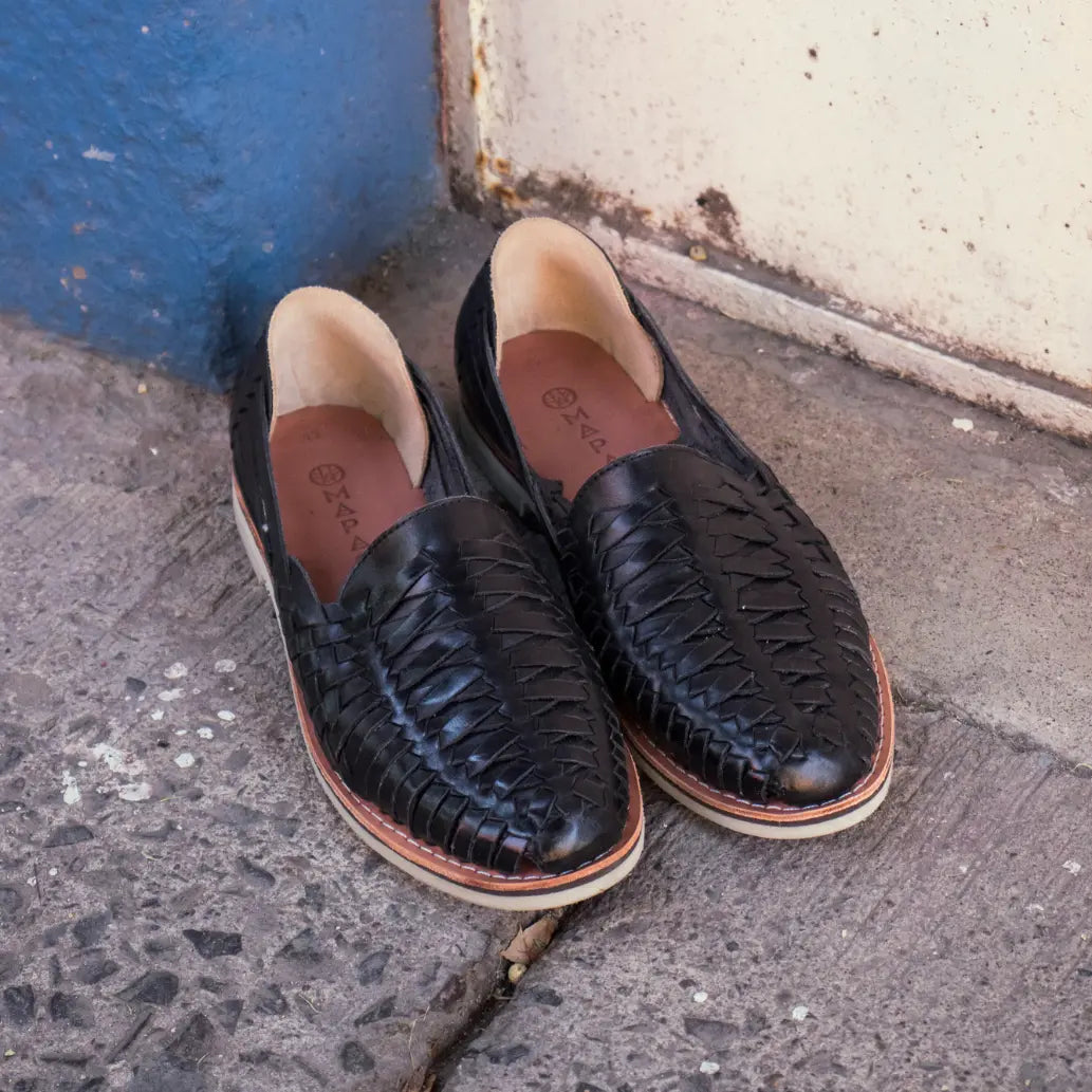 Les Mocassins Buena Vista Noir sont posé sur le sol, un mur bleu en arrière plan.