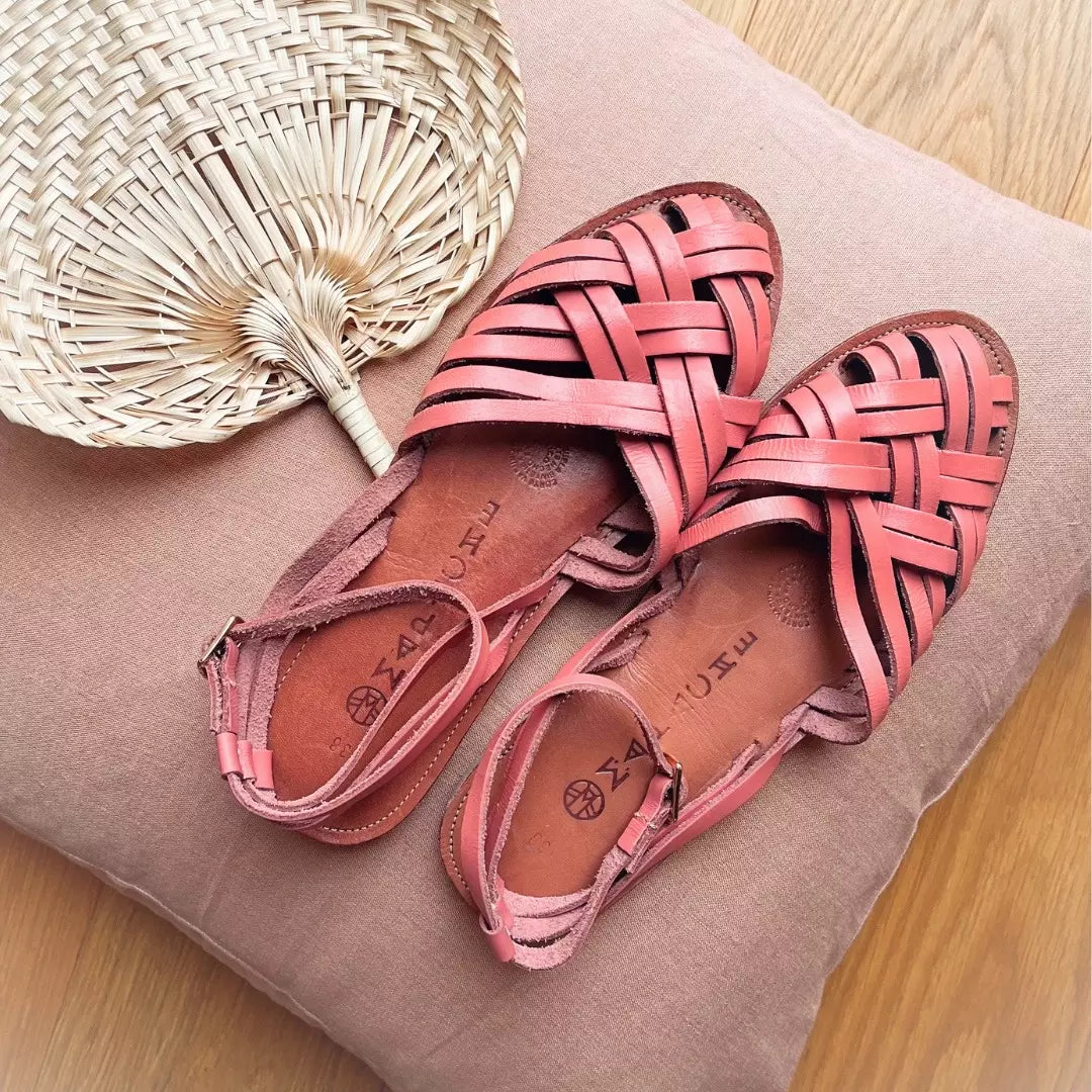 Les Sandales Mallorca Baby Pink sont posées sur un coussin rose avec un éventail tressé à côté.