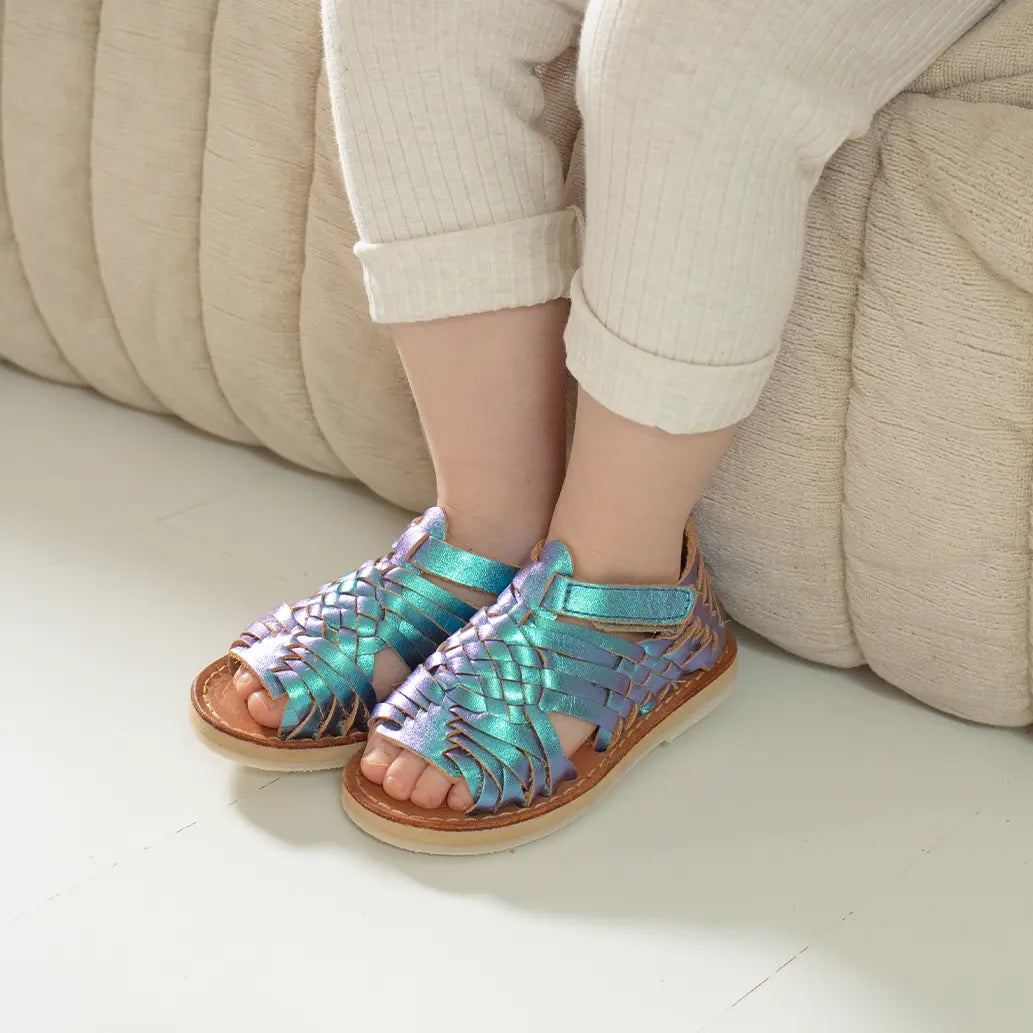 Une petite fille est assise sur un canapé beige et porte les Sandales Sandalita Blue Mermaid ainsi qu'un legging beige côtelé.