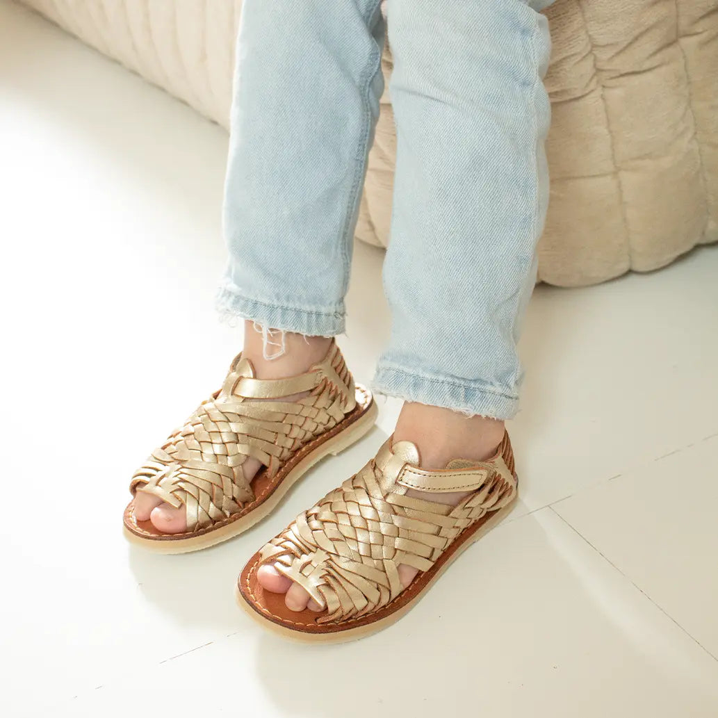 Une petite fille assise sur un canapé beige matelassé porte les Sandales Sandalita Champagne.